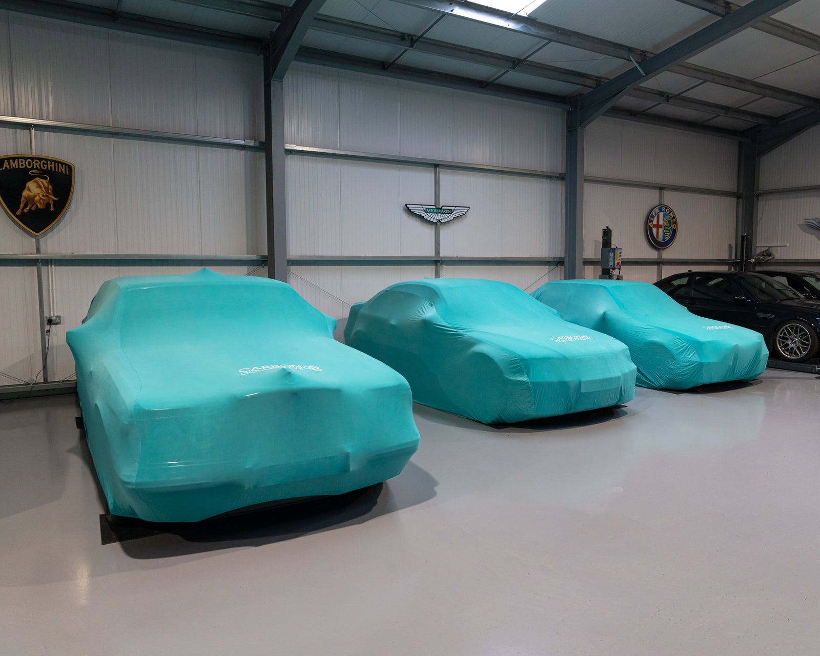 Three teal blue carbon collective indoor  car covers fitted on vehicles inside a storage facility